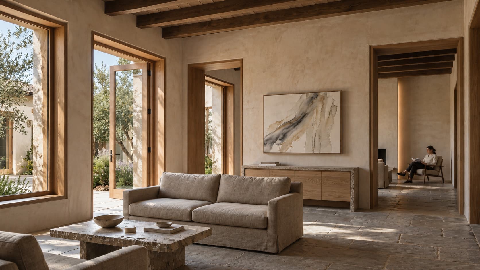 A lounge of lime plaster, oak beams and stone floors, open to a garden. A single abstract painting hangs above a low oak console, and a guest reads in the next room.